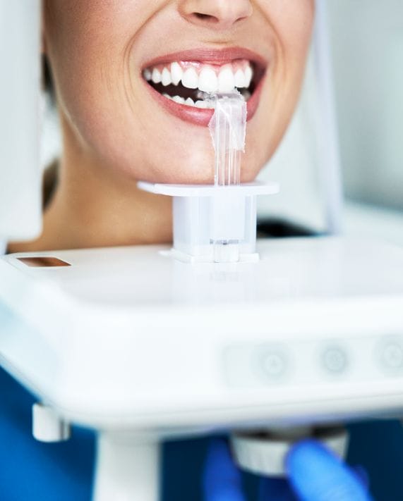 A smiling patient bites down on a plastic bite guide while undergoing a digital panoramic dental X-ray, a common procedure in general dentistry